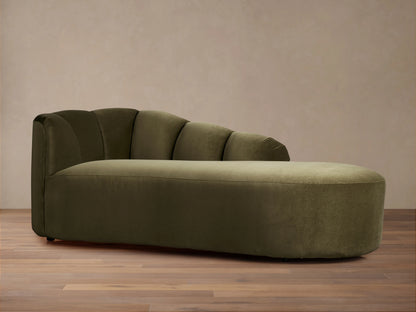Amira Daybed, an olive green velvet chaise lounge with a channel-tufted backrest & rounded edges, on a wooden floor.