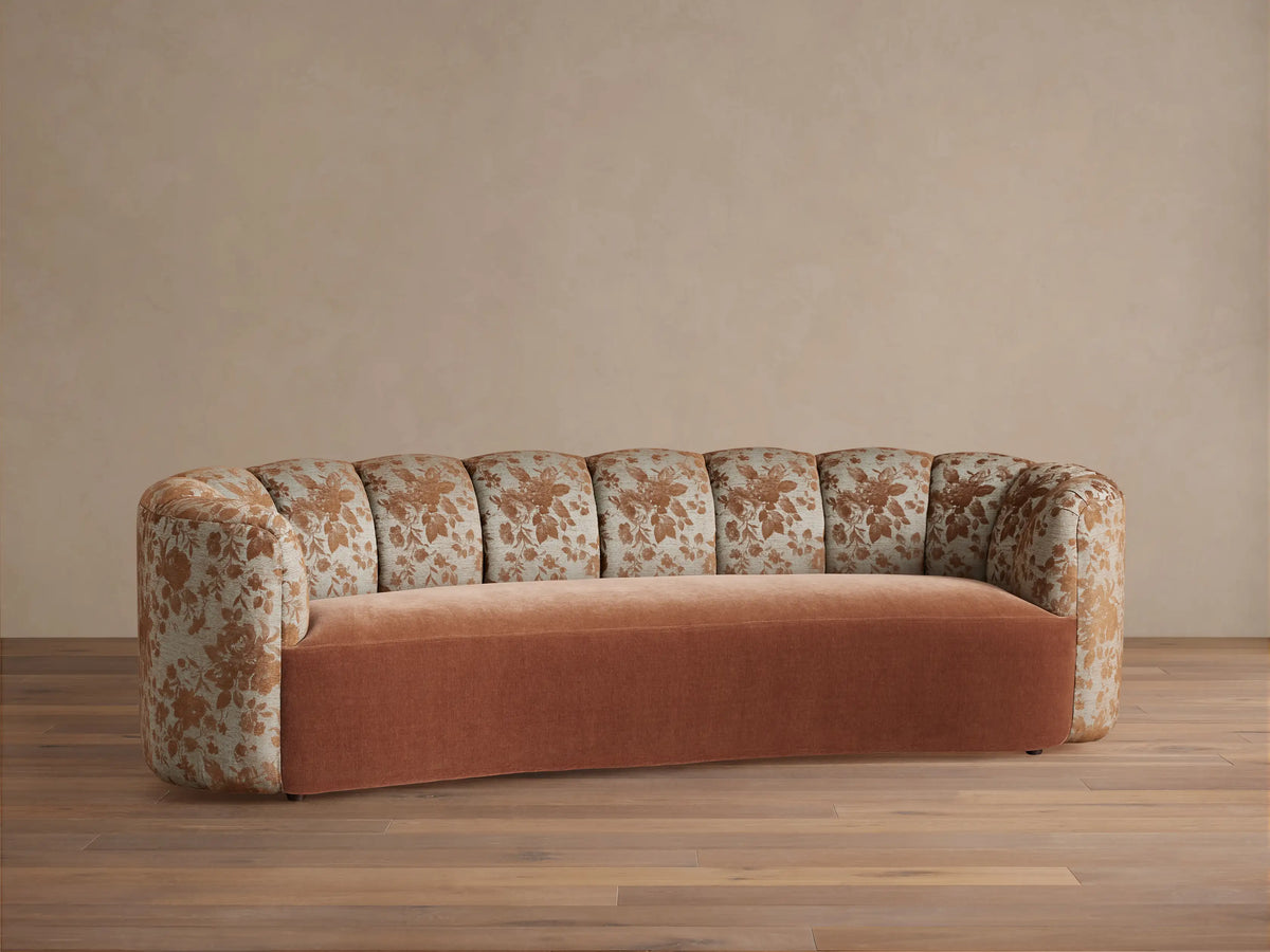 Amira Sofa: curved arms & channel-tufted back with brown floral pattern, solid cinnamon seat. Light wall, wood floor.