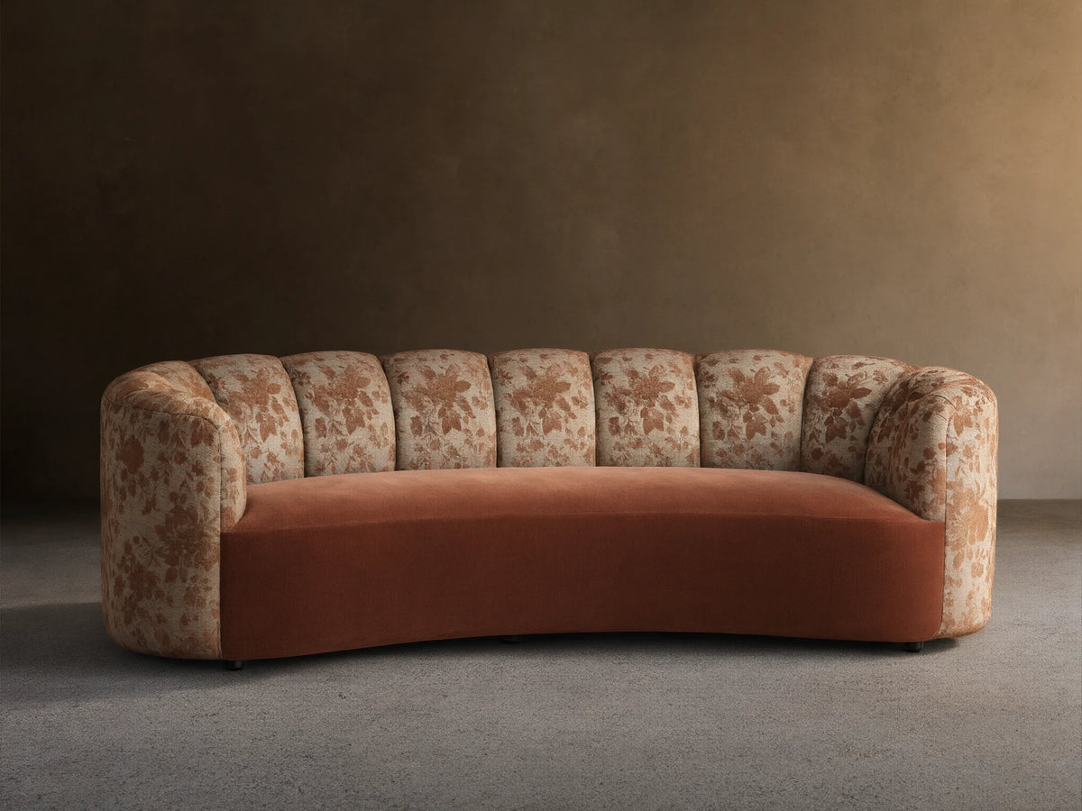 Amira Sofa: curved arms & channel-tufted back with brown floral pattern, solid cinnamon seat. Light wall, wood floor.