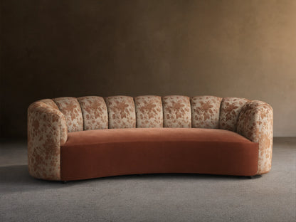 Amira Sofa: curved arms & channel-tufted back with brown floral pattern, solid cinnamon seat. Light wall, wood floor.