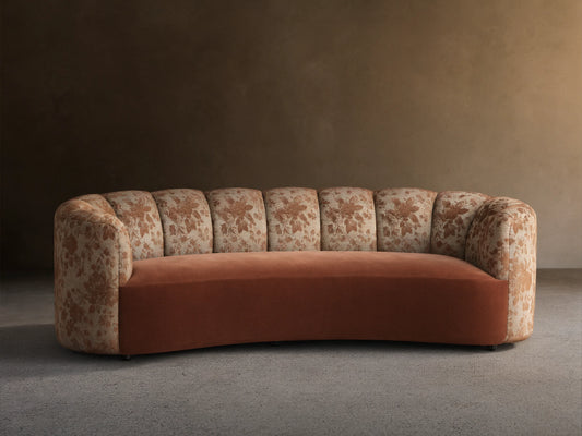 Amira Sofa: curved arms & channel-tufted back with brown floral pattern, solid cinnamon seat. Light wall, wood floor.