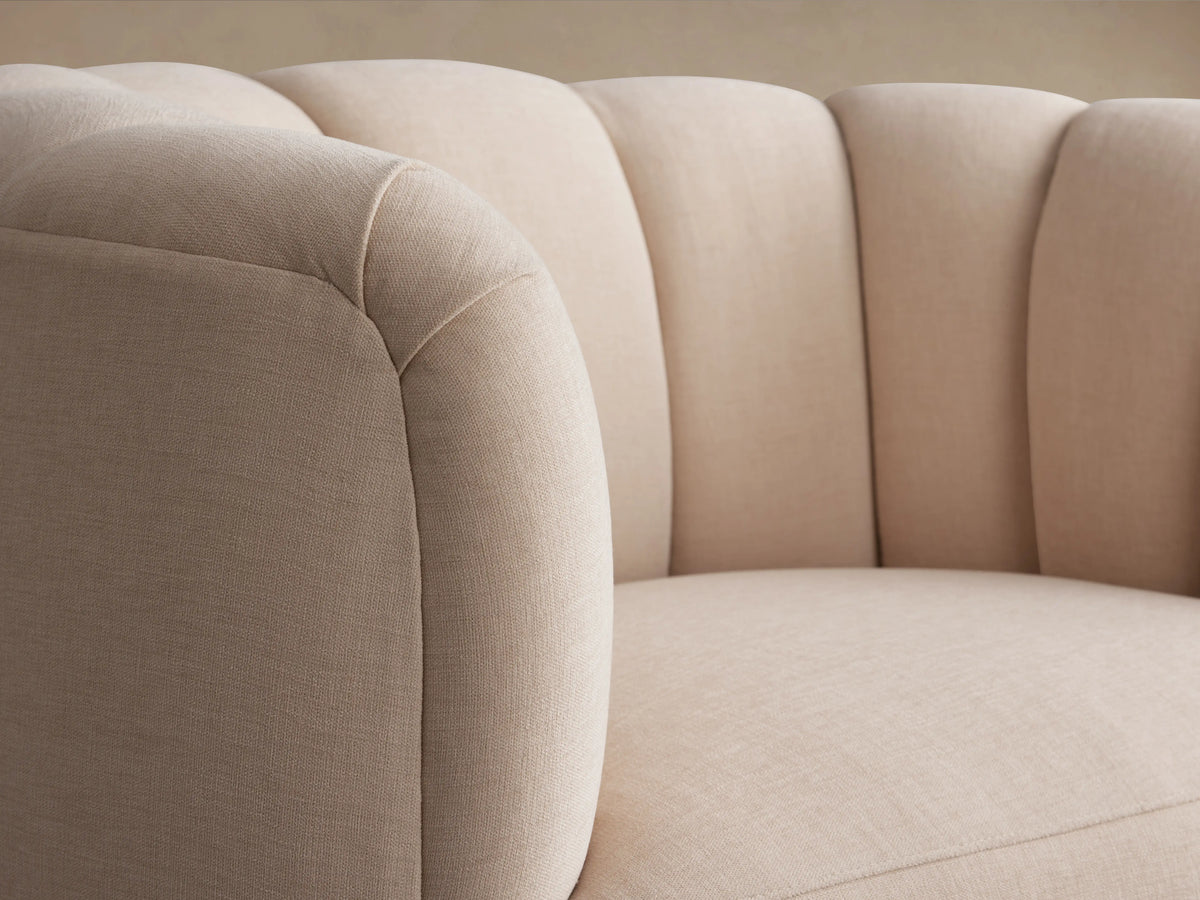 Amira Swivel Chair in blush fabric, featuring a rounded design with plush, tufted backrest and a 360-degree swivel base on a wooden floor.