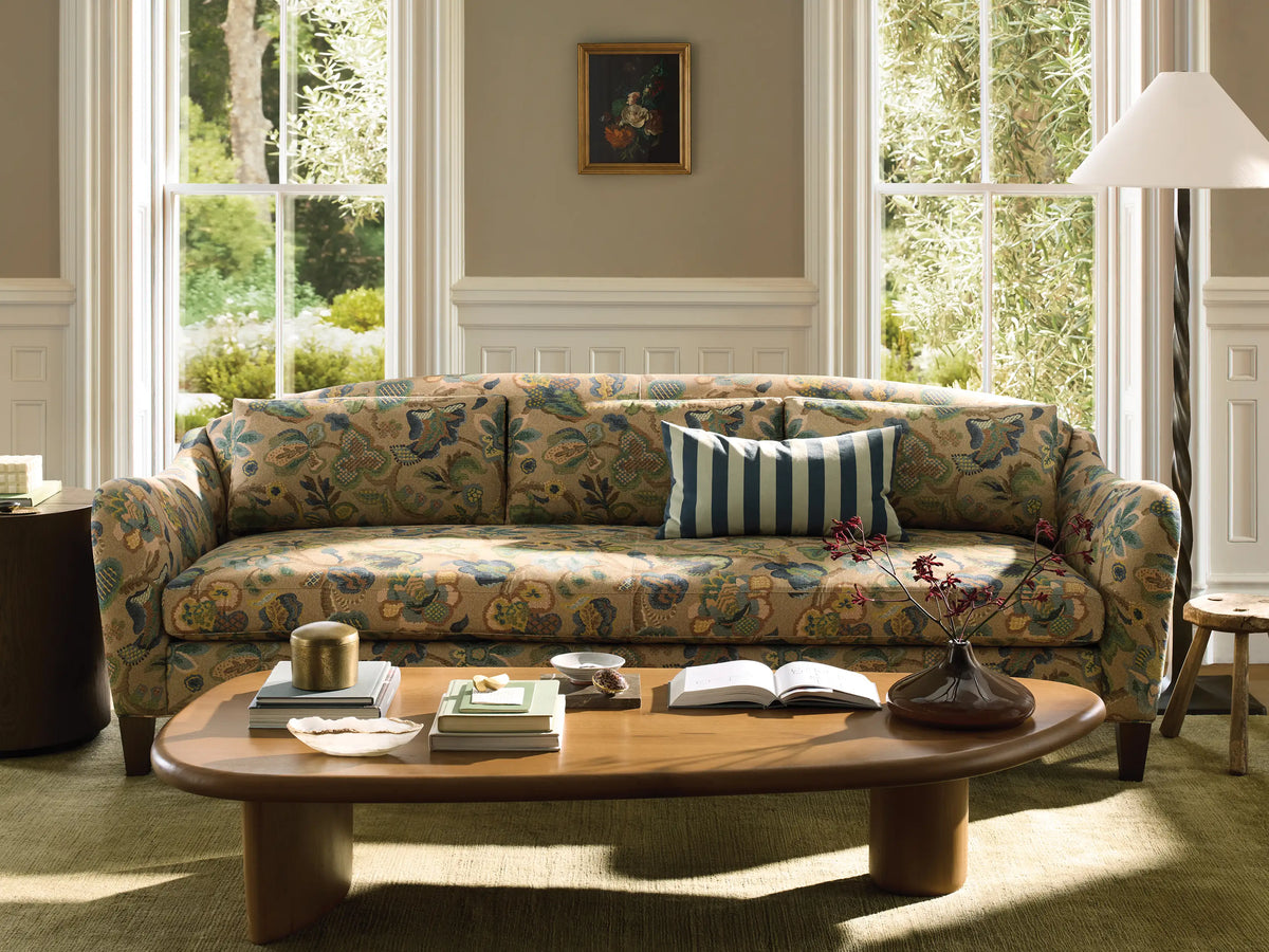 Front view of the Alina Sofa with beige upholstery in a multi-colored floral and paisley pattern, three back cushions, and dark wood legs.