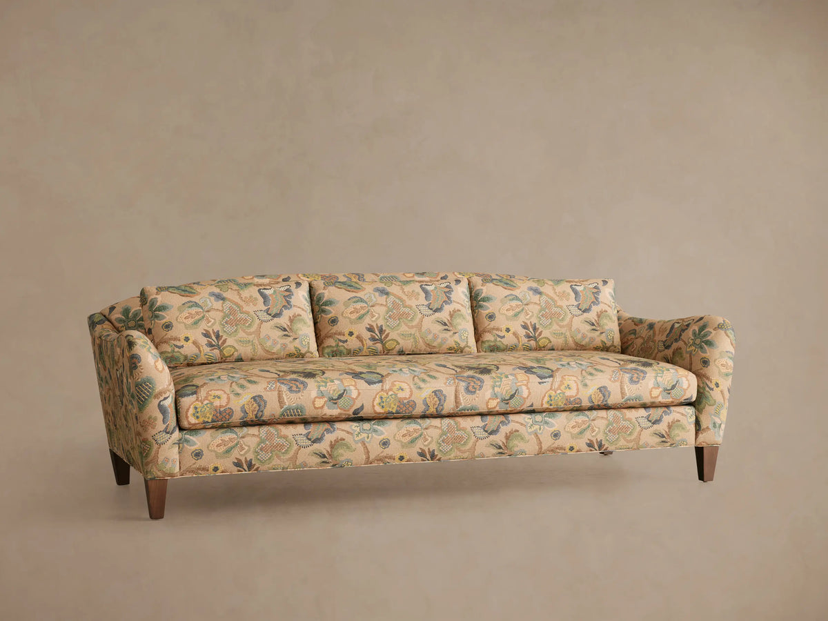 Front view of the Alina Sofa, upholstered in a beige fabric with an intricate blue and green floral pattern, in a living room.