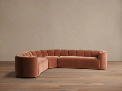 Front view of the terracotta velvet Amira Three-Piece Corner Sectional, featuring a curved design and channel-tufted backrest.