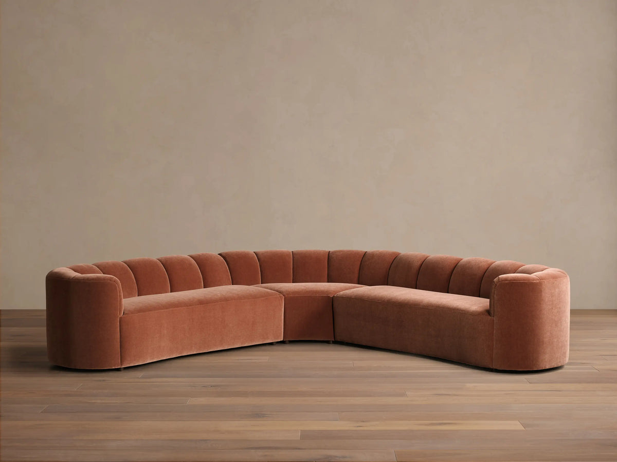 Front view of the terracotta velvet Amira Three-Piece Corner Sectional, featuring a curved design and channel-tufted backrest.