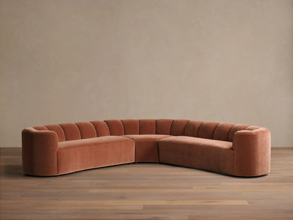 Front view of the terracotta velvet Amira Three-Piece Corner Sectional, featuring a curved design and channel-tufted backrest.