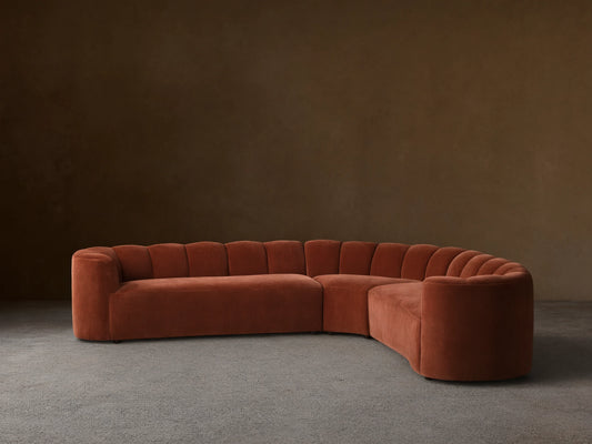 Front view of the terracotta velvet Amira Three-Piece Corner Sectional, featuring a curved design and channel-tufted backrest.