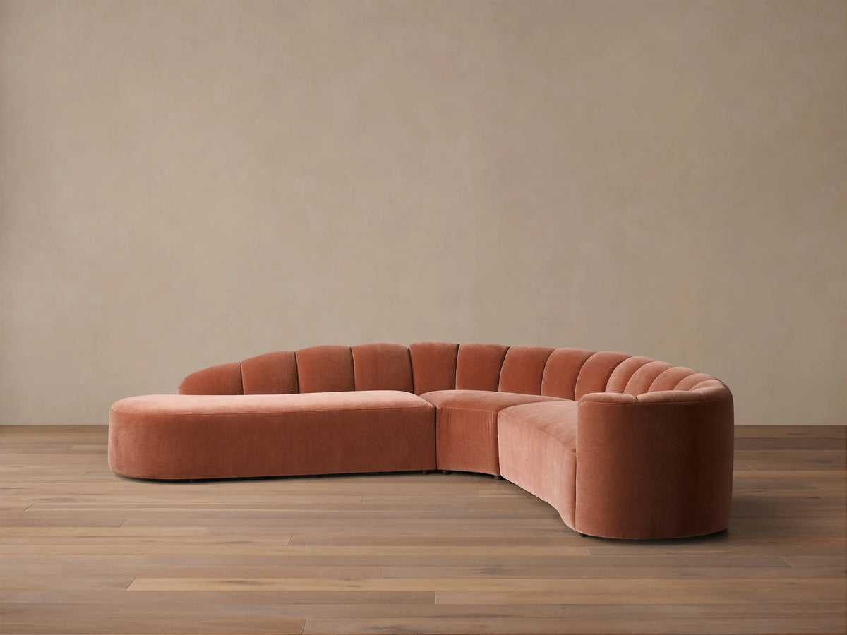 Front view of the terracotta pink Amira Three-Piece Bumper Sectional with a curved design and channel tufted back.