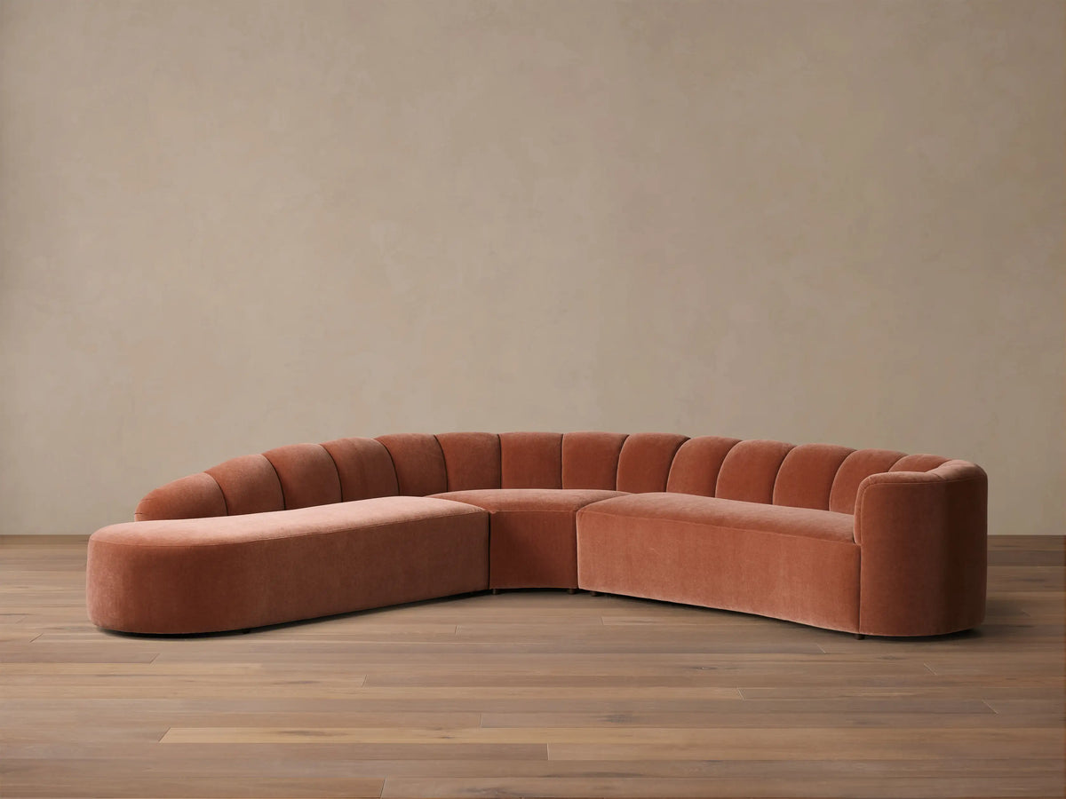 Front view of the terracotta velvet Amira Three-Piece Bumper Sectional, featuring a curved shape and channel tufted backrest.