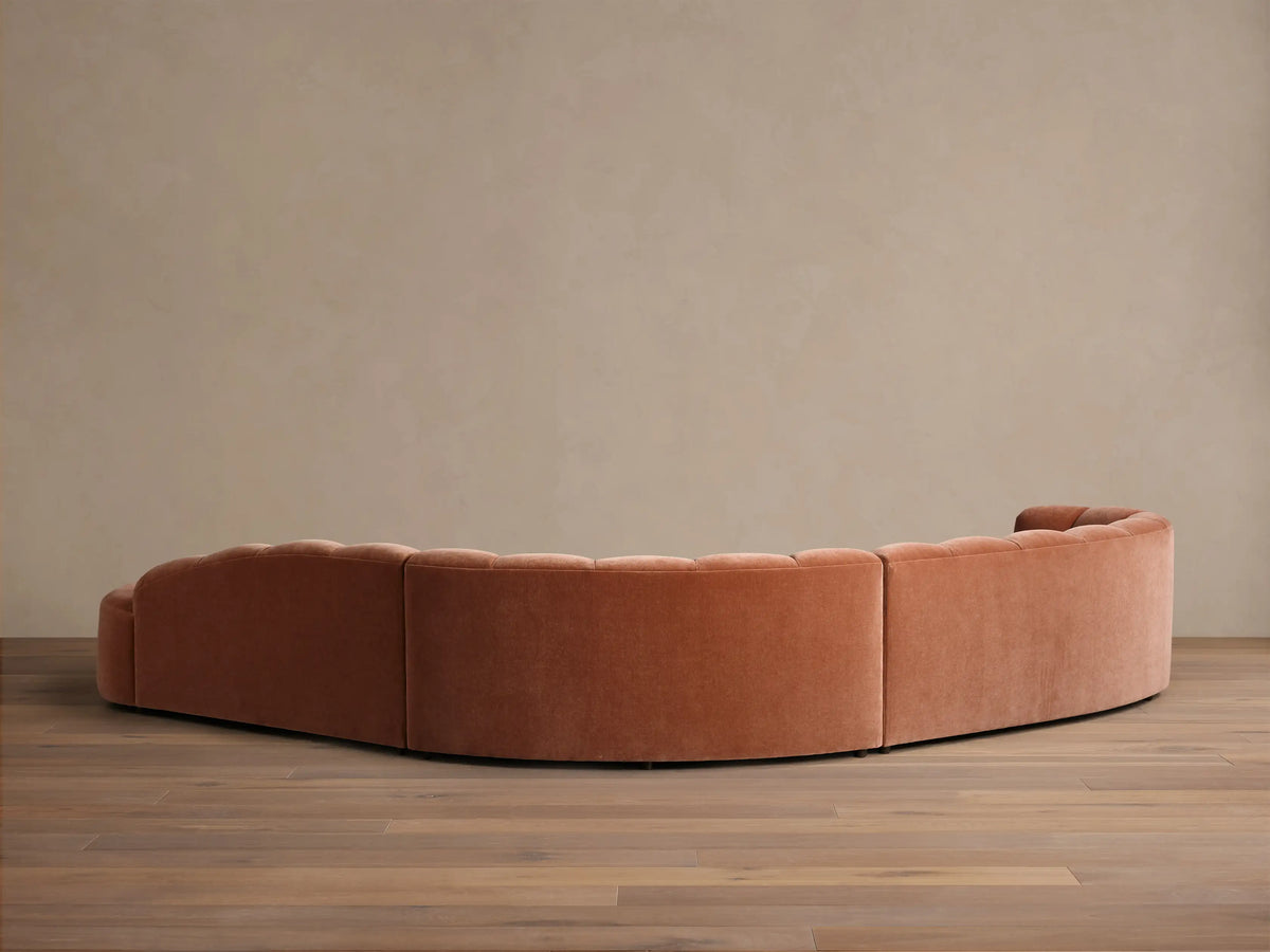 Rear view of the curved terracotta Amira Three-Piece Bumper Sectional with a tufted back.