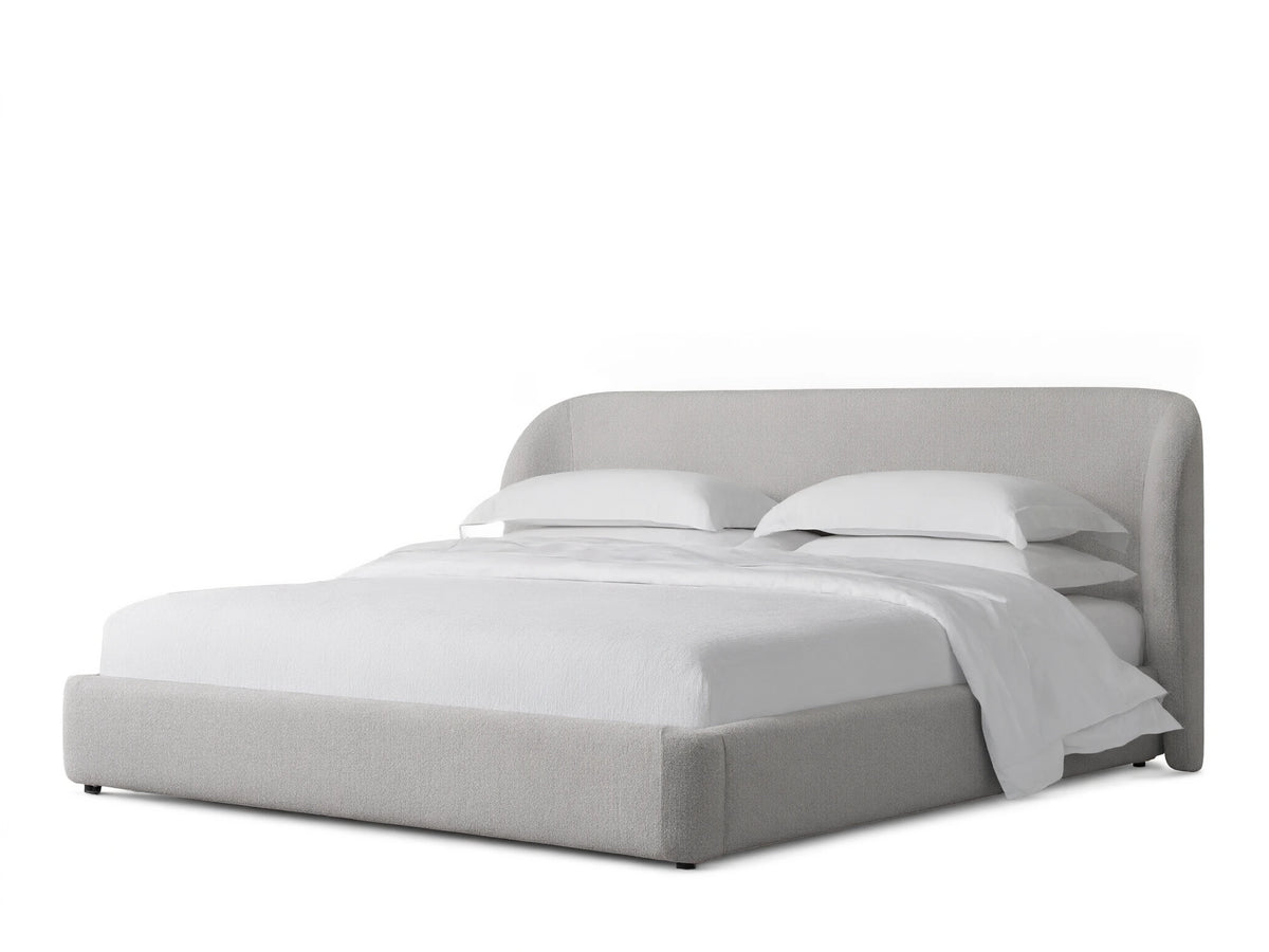 Adalynn Bed with a curved upholstered headboard and low-profile frame, in light beige fabric, set on wooden floor.