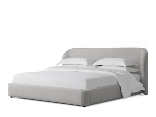 Adalynn Bed with a curved upholstered headboard and low-profile frame, in light beige fabric, set on wooden floor.