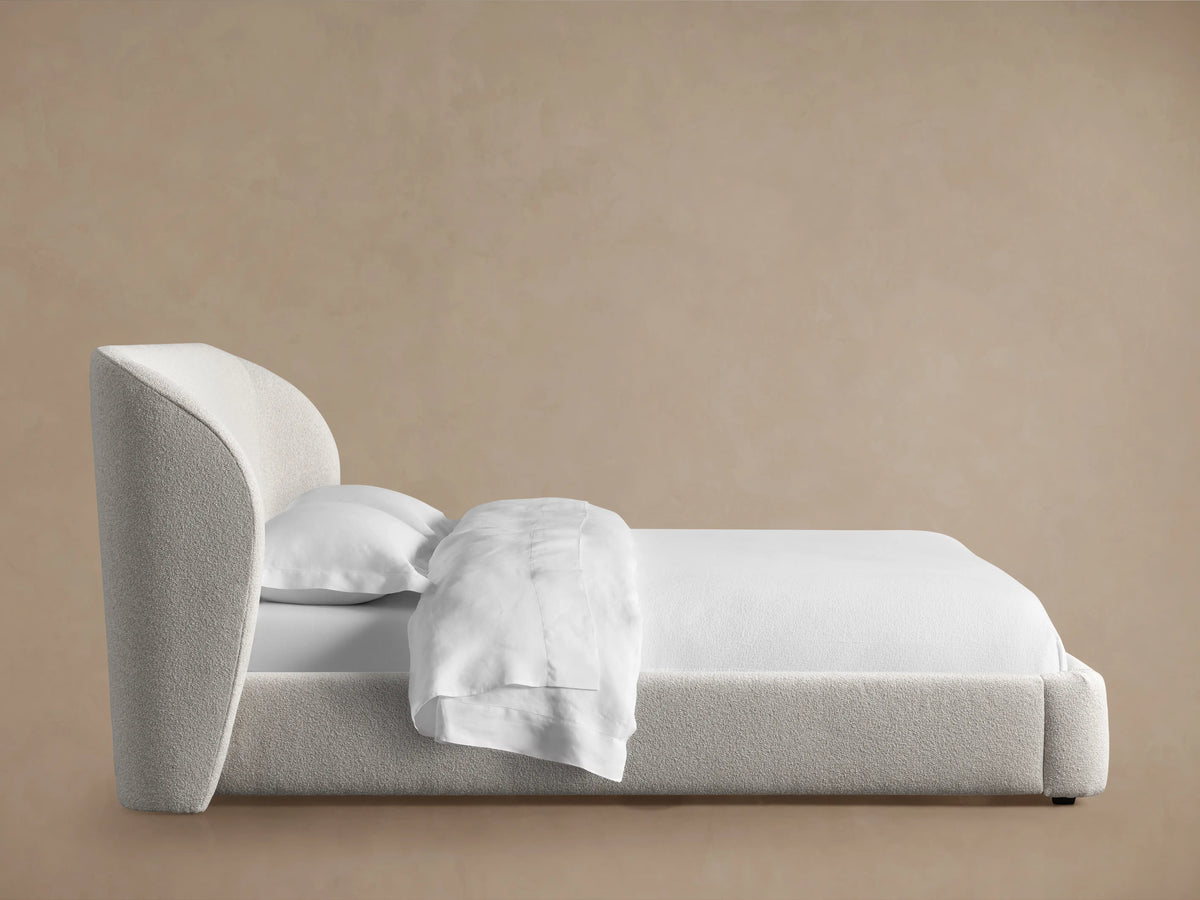 Close-up of the Adalynn Bed's upholstered headboard corner, showcasing its light gray textured fabric against a neutral background.