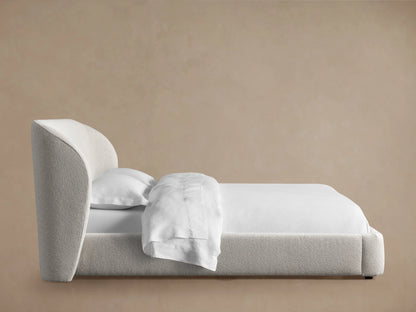 Close-up of the Adalynn Bed's upholstered headboard corner, showcasing its light gray textured fabric against a neutral background.