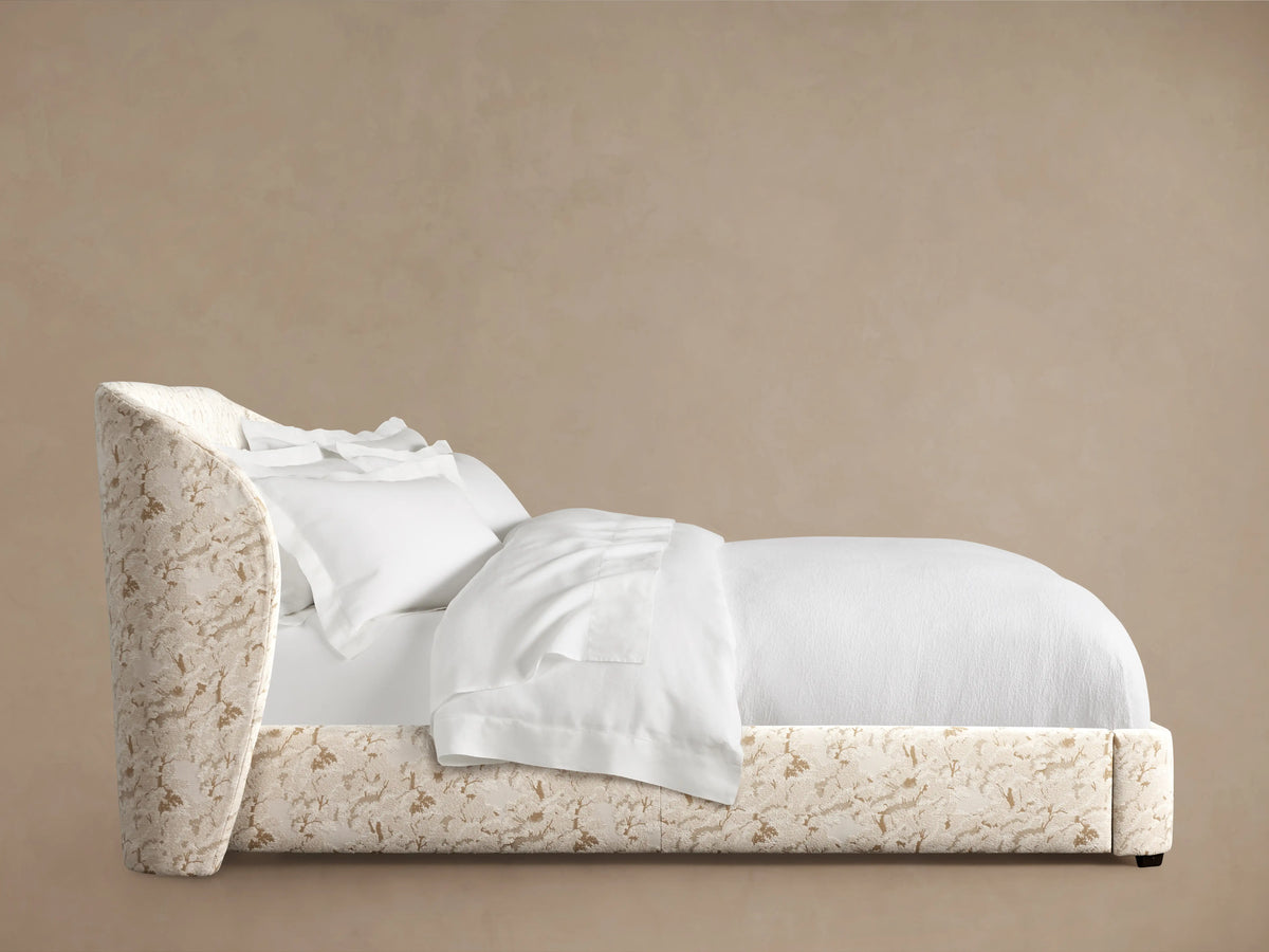 Adalynn Bed with an upholstered headboard in floral pattern, side view. White bedding, comforter, and pillows neatly arranged.