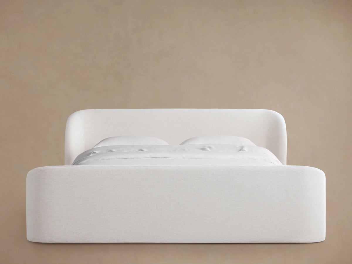 Adalynn Bed with High Footboard in white upholstery. The bed features a tall, curved headboard and footboard, set against a beige background.