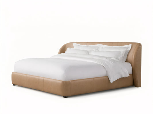 Adalynn Leather Bed in neutral tan leather, featuring a curved upholstered headboard, and dressed in white bedding on a wooden floor.