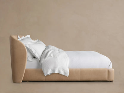 Adalynn Leather Bed in a light tan color with an upholstered headboard, white bedding, and pillows, viewed from the side.