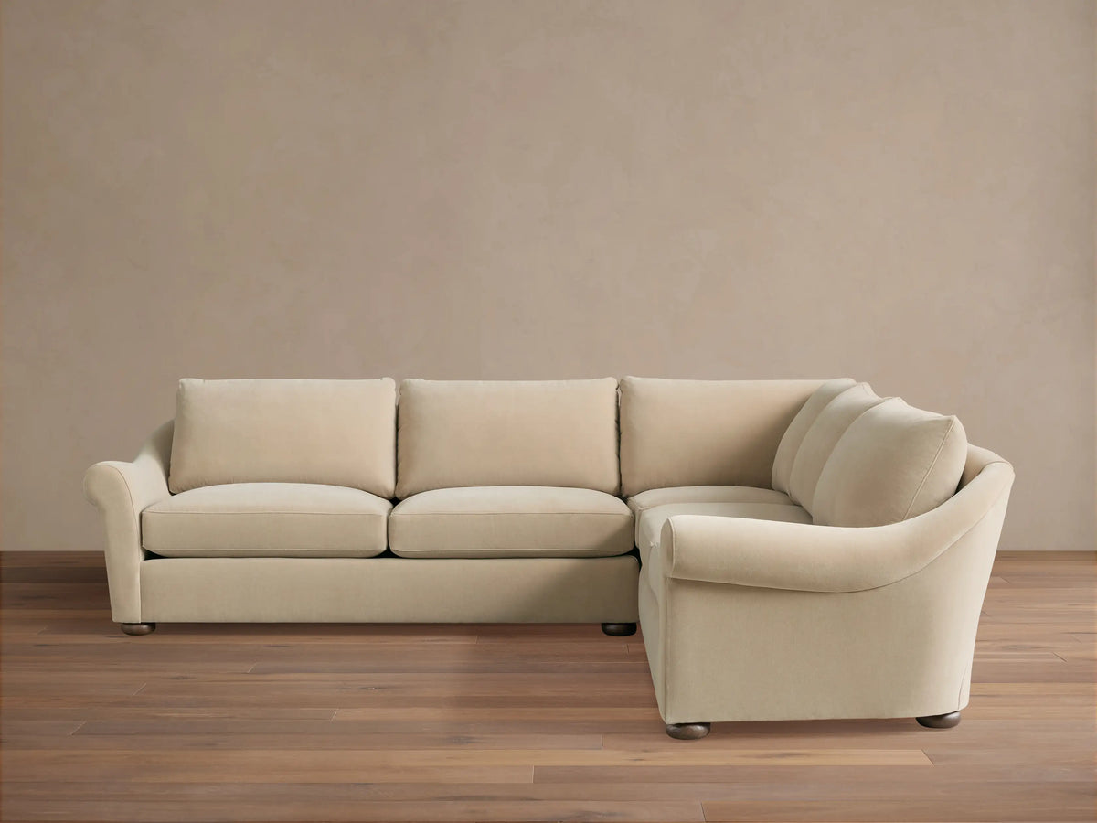 Archwood Three-Piece Corner Sectional in cream fabric, features rounded arms, plush back and seat cushions, on a wood floor.