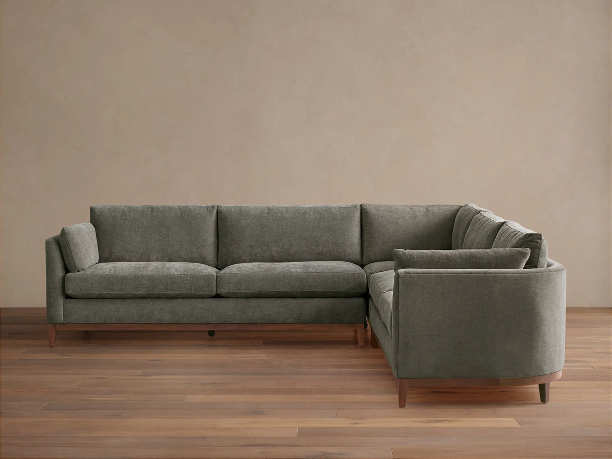 Bainbridge Three-Piece Corner Sectional, L-shaped, in deep moss green fabric, with exposed wood base & legs, on a wood floor.