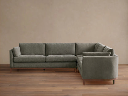 Bainbridge Three-Piece Corner Sectional, L-shaped, in deep moss green fabric, with exposed wood base & legs, on a wood floor.