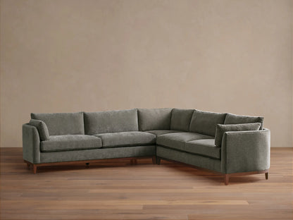 Bainbridge Three-Piece Corner Sectional, L-shaped, in deep moss green fabric, with exposed wood base & legs, on a wood floor.