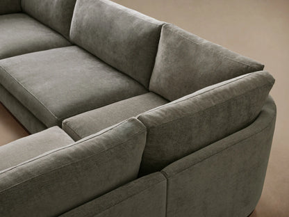 L-shaped Bainbridge Three-Piece Corner Sectional in muted olive green fabric with a visible wooden base on a wood floor.