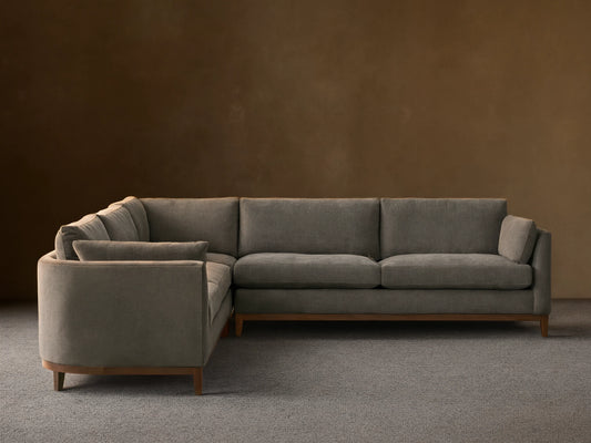 Bainbridge Three-Piece Corner Sectional, L-shaped, in deep moss green fabric, with exposed wood base & legs, on a wood floor.