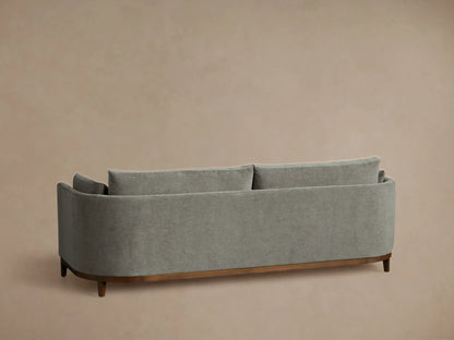 Angled close-up of the Bainbridge Sofa, featuring textured gray fabric, curved armrest with cushion, and dark wooden base.