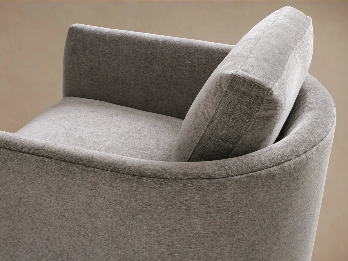 Bainbridge Chair in gray fabric, front view, features plush seat and back cushion. Wooden legs on a light wood floor, against beige wall.