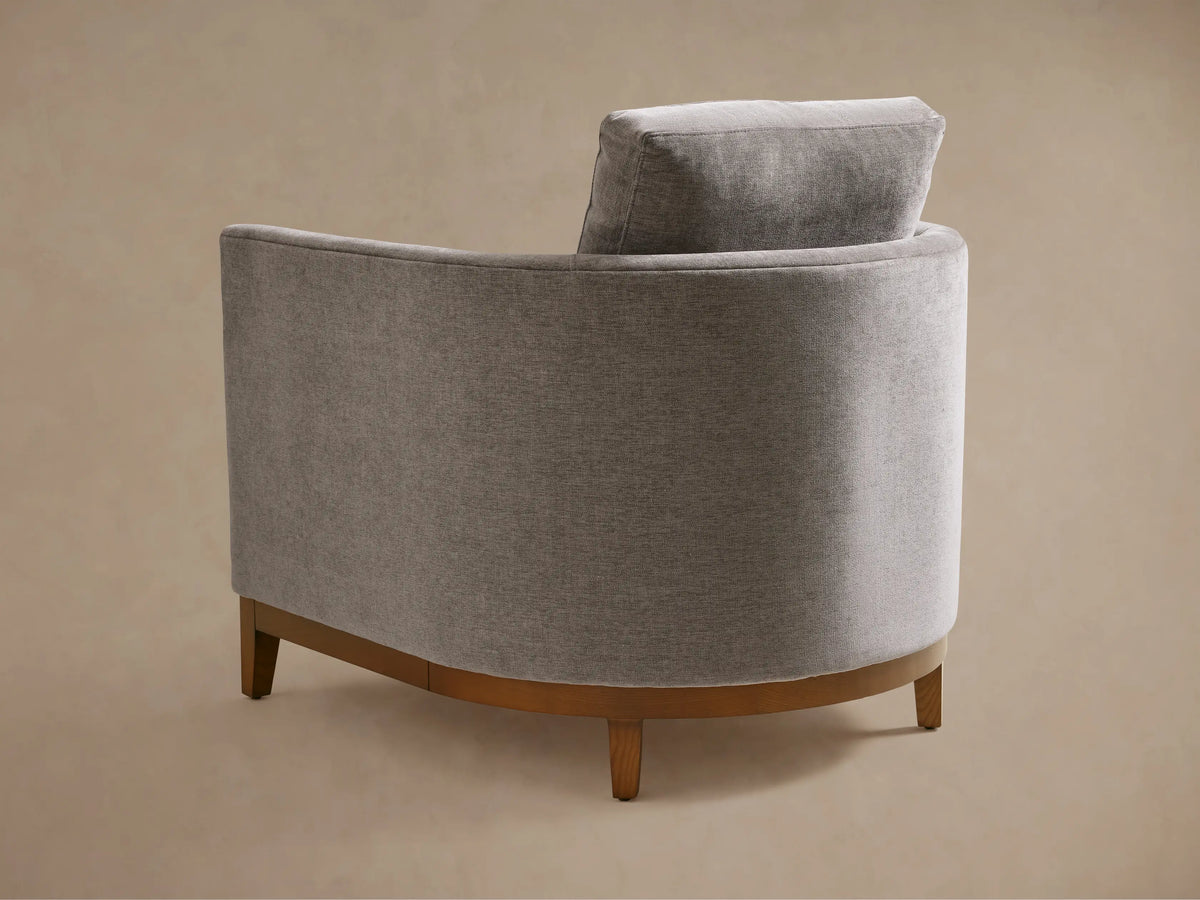 Bainbridge Chair in light gray fabric, featuring a curved back, plush seat, and armrest. Upholstery shows fine texture detail.