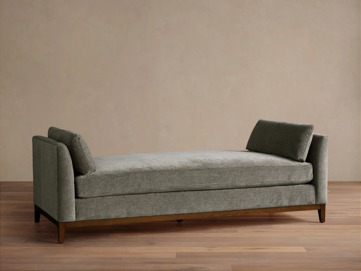 Bainbridge Daybed, gray-green textured fabric, two angled back cushions, dark wood base on wood floor.