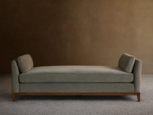 Bainbridge Daybed, gray-green textured fabric, two angled back cushions, dark wood base on wood floor.