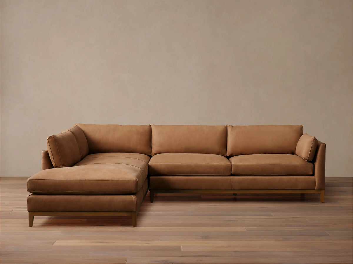 Bainbridge Two-Piece Bumper Sectional in warm brown leather, L-shaped with a left-hand chaise. Sits on a wooden floor.
