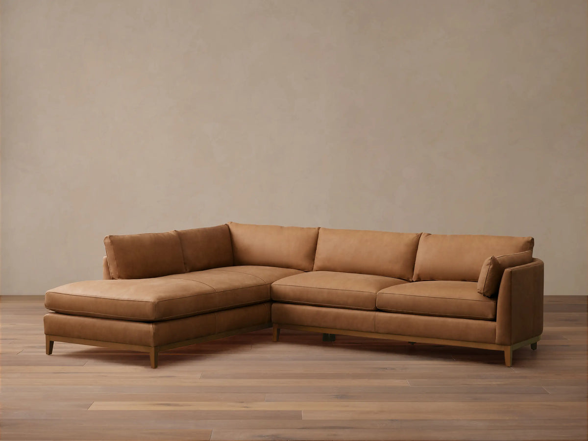 Bainbridge Two-Piece Bumper Sectional in warm brown leather, L-shaped with a left-hand chaise. Sits on a wooden floor.