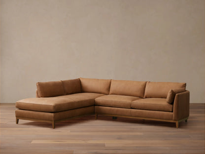 Bainbridge Two-Piece Bumper Sectional in warm brown leather, L-shaped with a left-hand chaise. Sits on a wooden floor.