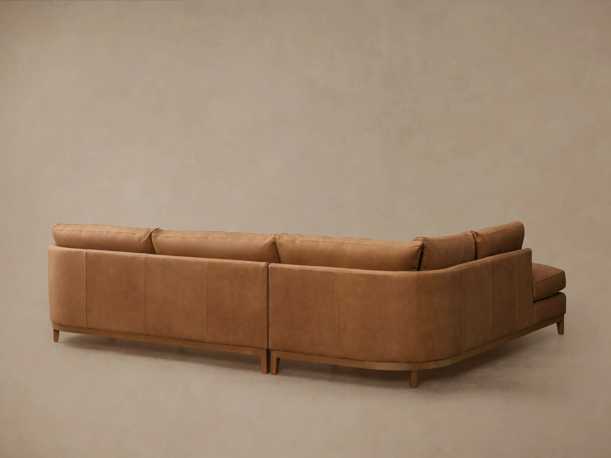 Close-up of Bainbridge Leather Two-Piece Bumper Sectional chaise. Light brown leather with visible stitching and a wooden base.