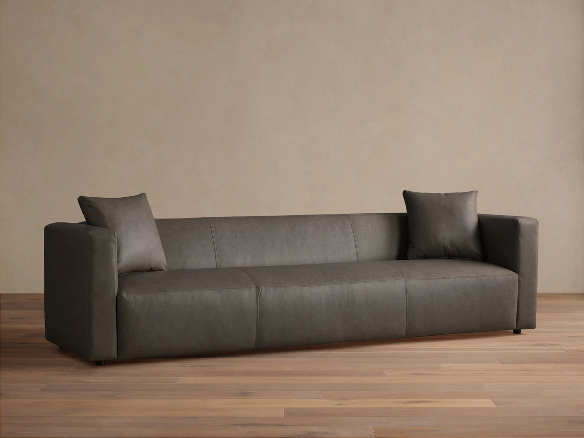 Front view of the dark gray Brady Leather Sofa, featuring fixed cushions, square arms, and two matching toss pillows.