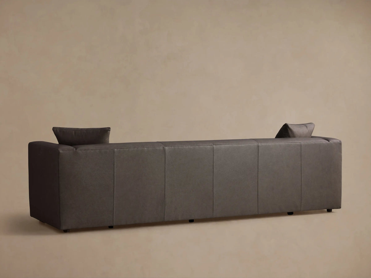 Close-up of the charcoal leather Brady Leather Sofa, showing visible stitching, a square armrest, and a matching toss pillow.