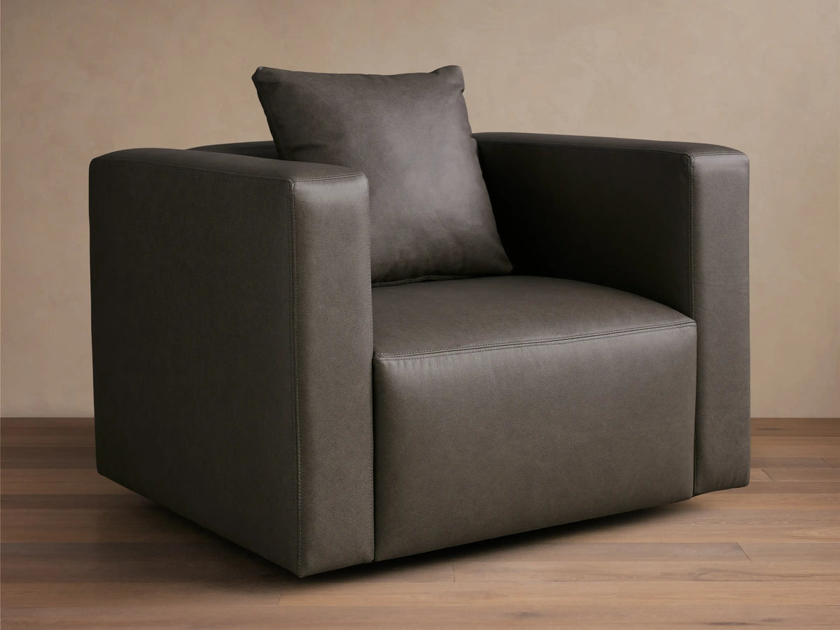 Front-angled view of a Dark Gray Brady Leather Swivel Chair with square arms and a matching toss pillow.