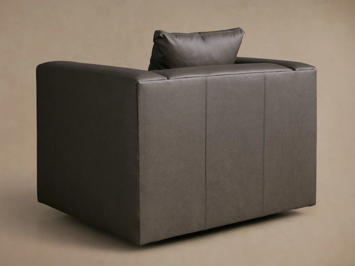 Close-up of the dark gray leather Brady Leather Swivel Chair, showing square arms, visible stitching, and a matching toss pillow.