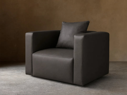 Front-angled view of a Dark Gray Brady Leather Swivel Chair with square arms and a matching toss pillow.