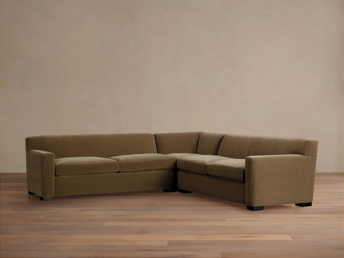 Bronte Three-Piece Corner Sectional in muted olive green fabric, forming an L-shape, on a wood floor against a beige wall.