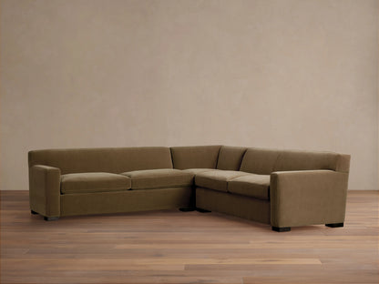 Bronte Three-Piece Corner Sectional in muted olive green fabric, forming an L-shape, on a wood floor against a beige wall.