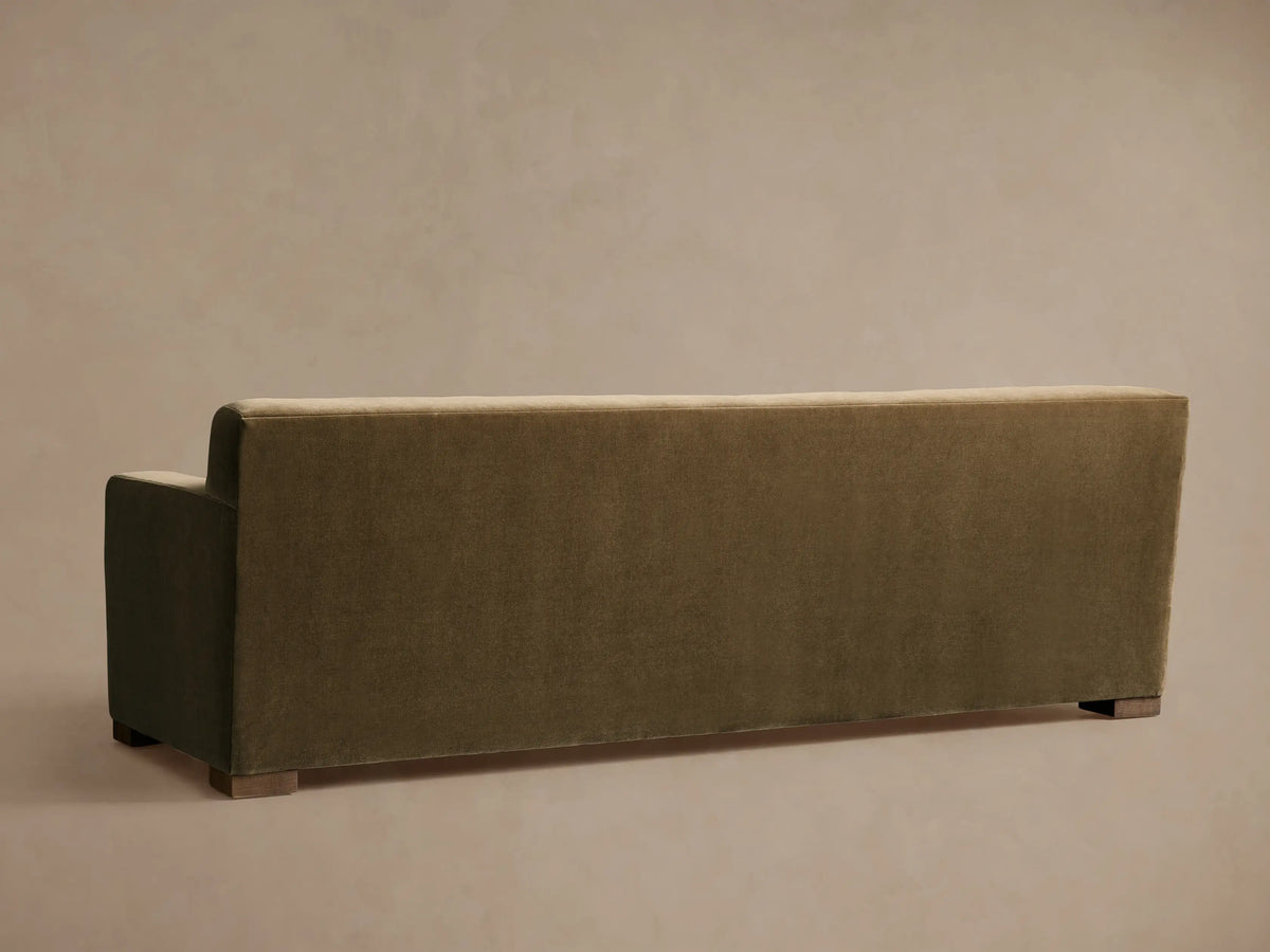 Rear view of an olive green Bronte Bench-Seat Sofa, featuring a low back, a partial left arm, and dark wooden block feet.