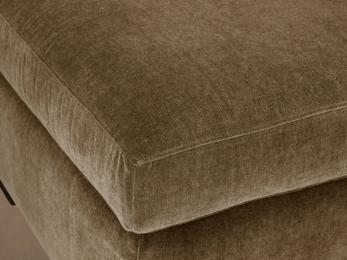 Bronte Ottoman: plush, rectangular, muted olive green fabric. Soft top cushion, dark block feet on a wood floor.