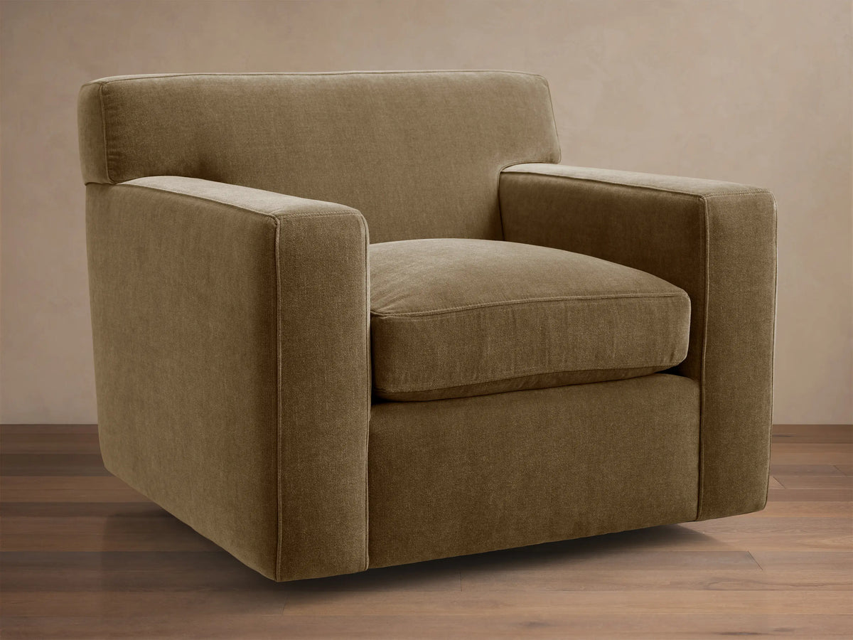 Bronte Swivel Chair, upholstered in textured, earthy brown-green fabric, with clean lines, wide squared arms, on a wood floor.
