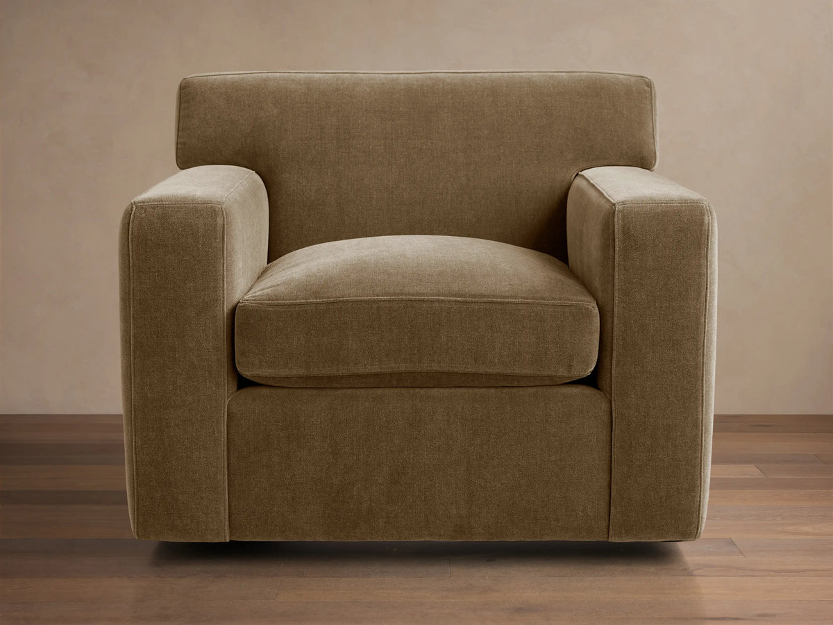 Bronte Swivel Chair, upholstered in textured, earthy brown-green fabric, with clean lines, wide squared arms, on a wood floor.