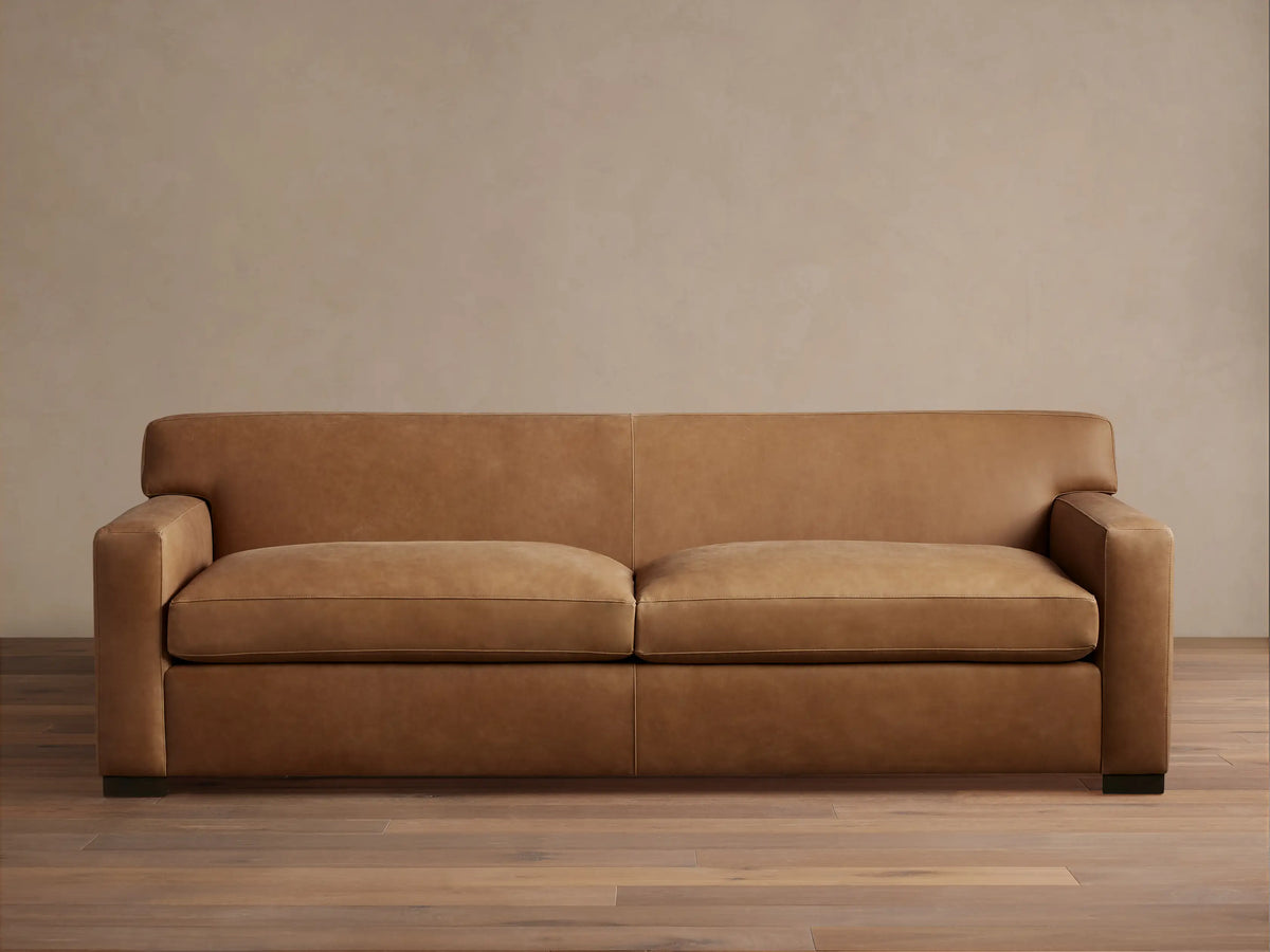 Bronte Leather Sofa in brown leather with a sleek design, featuring straight arms and deep seat cushions on a hardwood floor.